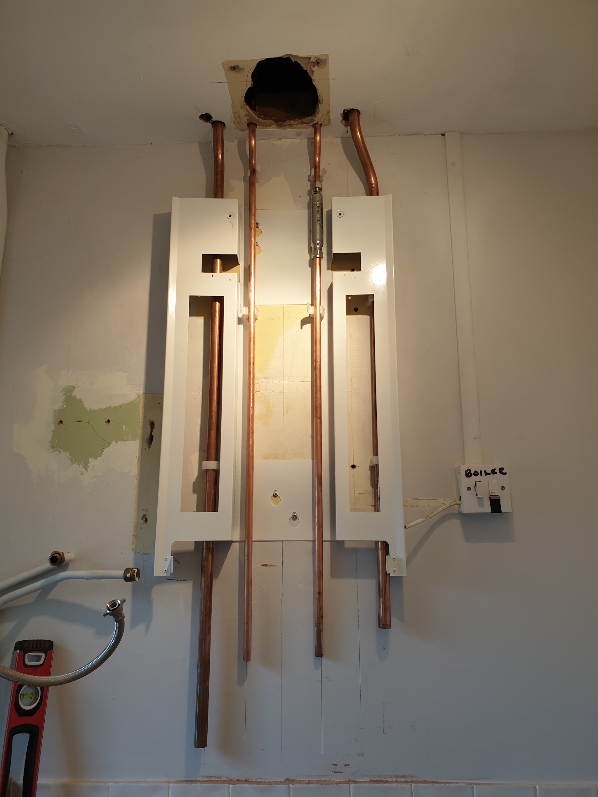 A boiler mounting frame and new copper pipework on the wall, ready for the boiler to go on
