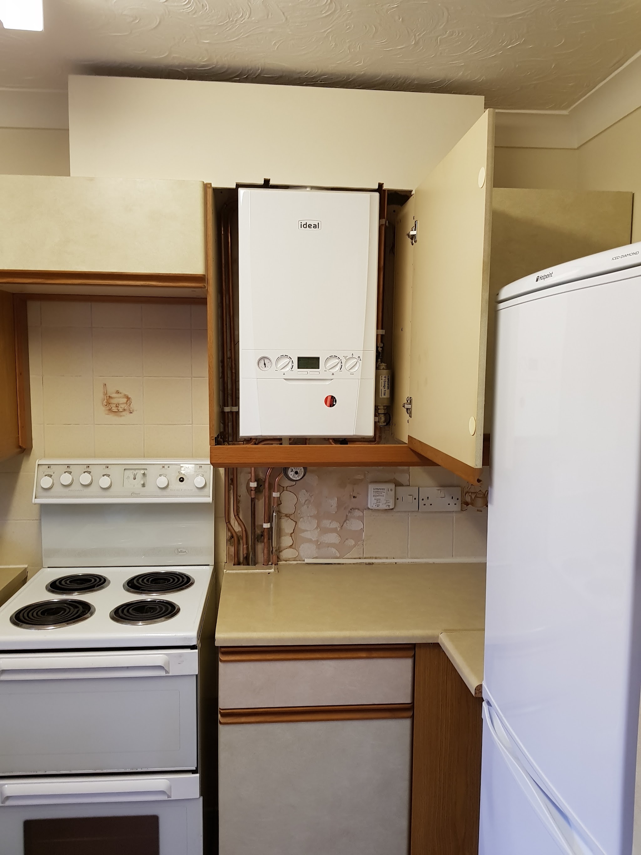A white Ideal boiler fitted inside a kitchen wall cupboard above an electric cooker