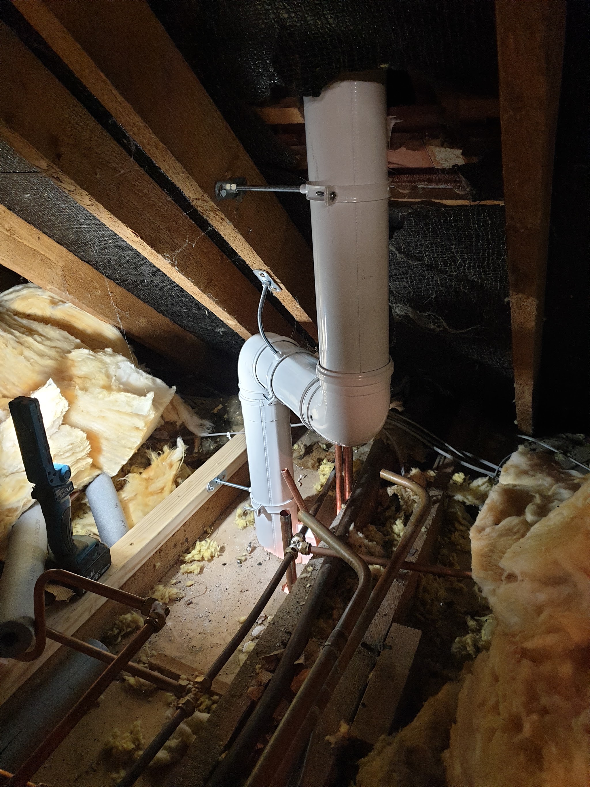 A white boiler flue running up through a loft between the rafters